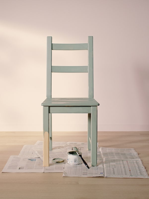 漆成浅绿色的IVAR椅子站在旧报纸上，在一个空房间里，浅木地板和浅粉红色的墙壁。
