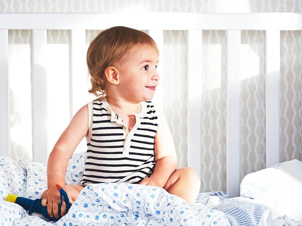 Malo dete sedi u belom SUNDVIK krevecu, ija je jedna strana skinuta, s GULSPARV posteljinom sa arom u obliku borovnice。