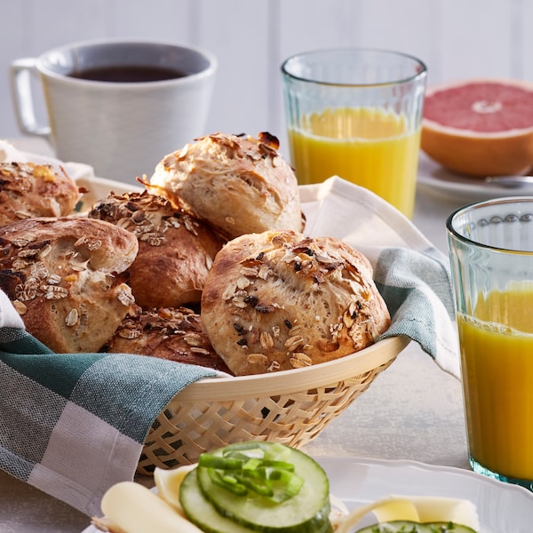 Mand met broodjes gemaakt met HJÄLTEROLL muesli op een ontbijttafel, naast even kop koffie, even glass sap en even half葡萄柚。