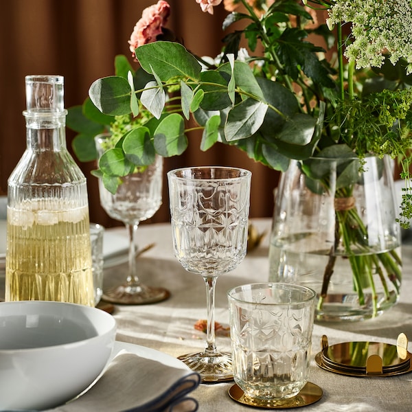 SÄLLSKAPLIG glasskaraffel, glass, vingglass og blomster i en glassvase på et bord med naturfarget duk。
