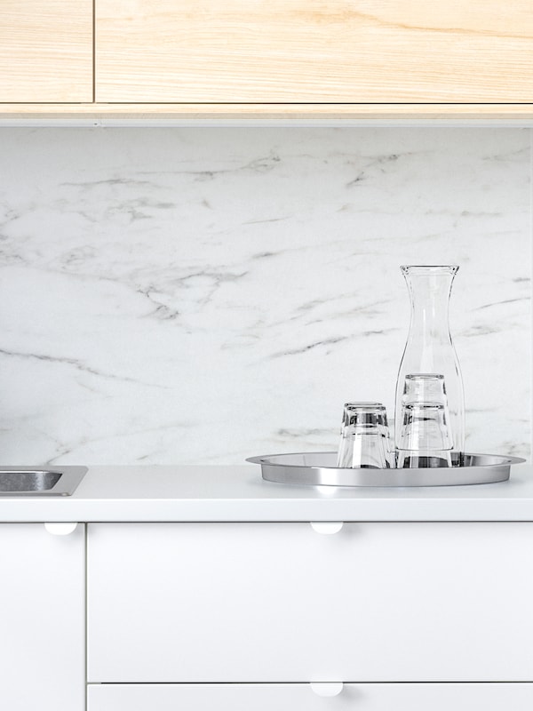 SIBBARP墙板在白色大理石效果方面的厨房白色和桦木、一盘戴眼镜和一个玻璃水瓶。