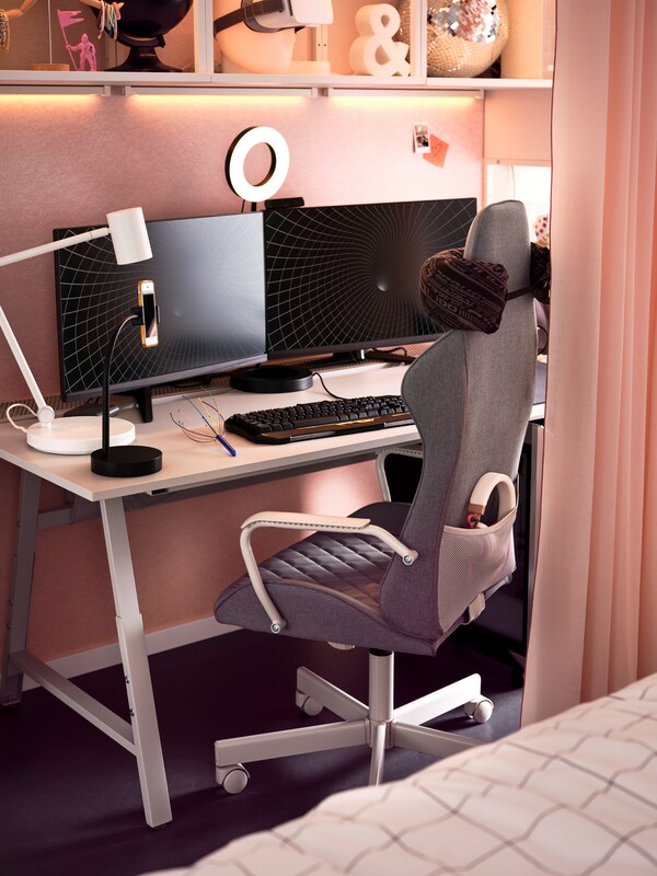 Szary fotel gamingowy UTESPELARE ustawiony przed szarym biurkiem gamingowym z dwoma monitorami, lampąbiurkową,lampąpierścieniową我klawiaturą。