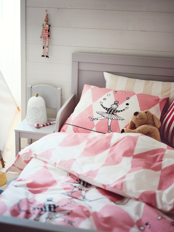 灰色SUNDVIK可扩展的高端床上覆盖着粉红色和白色BUSENKEL床单用软玩具在床上。