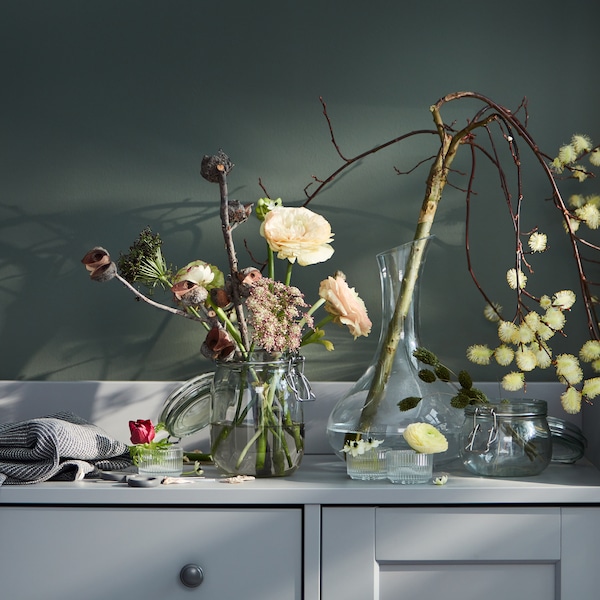 一个灰色HAUGA餐具柜装满了各种vase-and-flower组合,包括一个STORSINT玻璃水瓶。