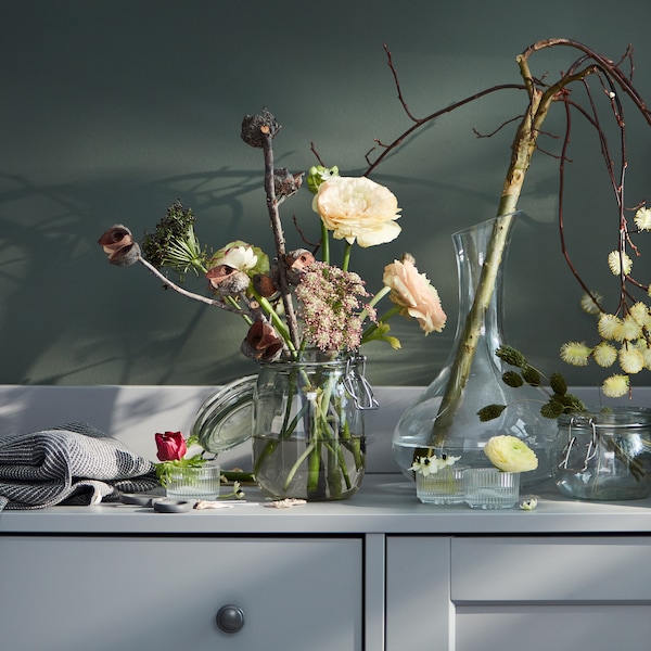 一个灰色HAUGA餐具柜与各种鲜花在玻璃瓶中,茶蜡持有者和透明玻璃STORSINT玻璃水瓶。