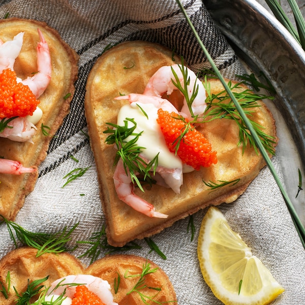 三个心形的VAFFLOR虾仁蛋奶烘饼,蛋黄酱,海藻珍珠和莳萝厨房毛巾在盘子里。
