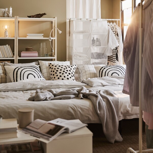 两个LYCKSELE lova沙发床与灰色的床上用品和图案的枕头,加上白色的咖啡桌和白色衣服架子。