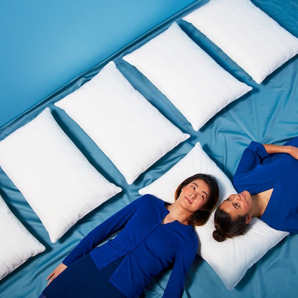 两个人穿深蓝色的衣服躺在蓝色的地板上,头在枕头上,旁边一排其他的枕头。