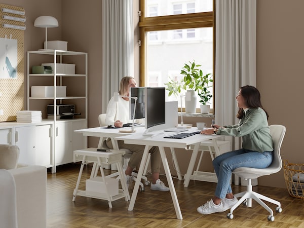 两个女人在一个工作区与两个白人TROTTEN桌子,两个LANGFJALL办公室椅子和电脑屏幕。