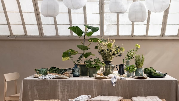 玻璃屋顶下表亚麻桌布,盘子,和大量的植物和分支在植物锅和花瓶。