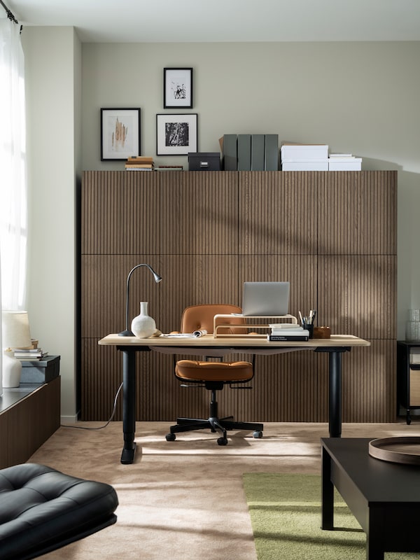 V jemne slnkom osvetlenej miestnosti je stôl BEKANT, zlatohnedá kancelárska stolivka ALEFJÄLL a pri stene skrinky s drevenými dvierkami。