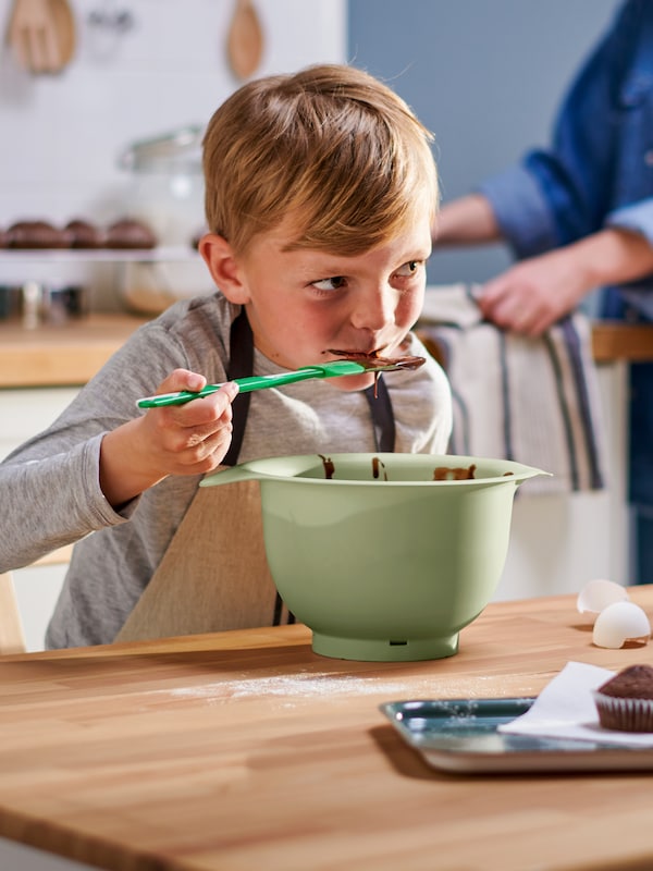 有绿色GUBBRORA抹刀,一个孩子在一个MARIATHERES围裙从绿色的碗吃巧克力蛋糕面糊。